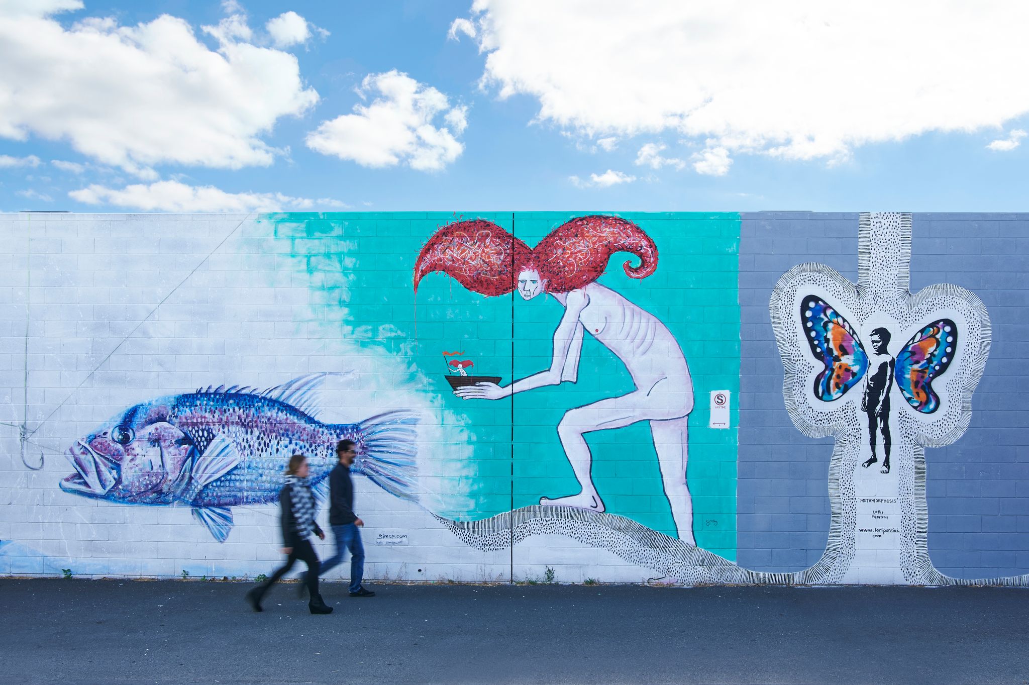 2 people walk by a wall with street art