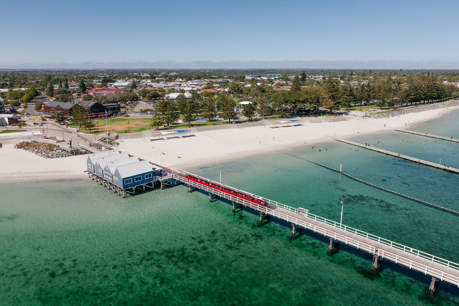 An aerial image of Busselton Jetty with a red jetty train and blue water