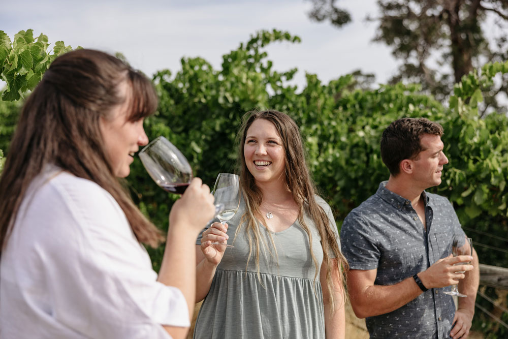 Three people smile while drinking wine in a vineyard in Ferguson Valley