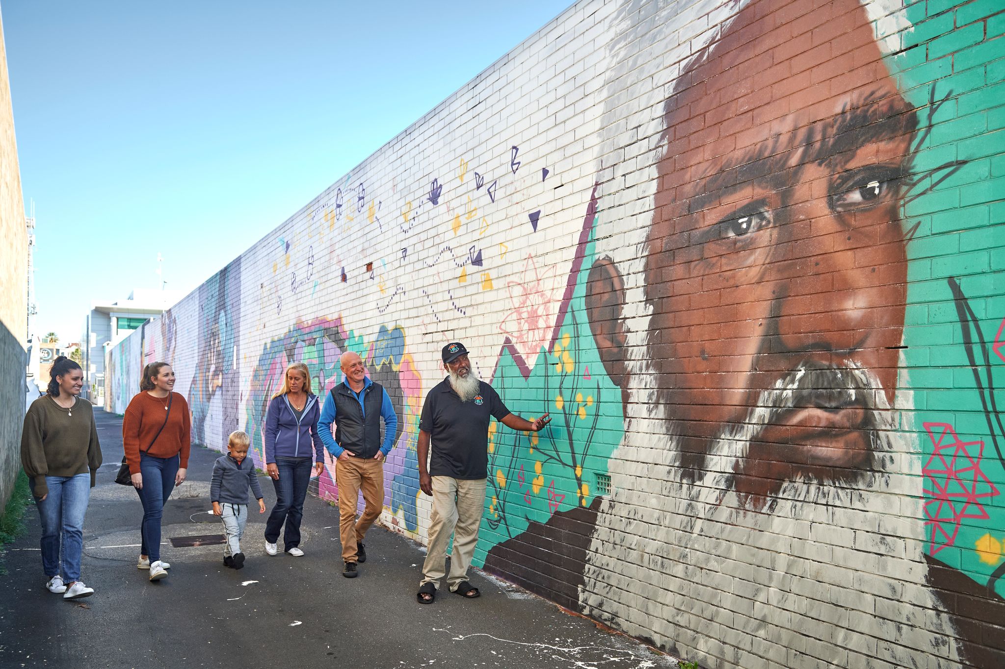 A group of people walk down an alleyway next to street art with a cultural guide on an Aboriginal Street Art tour in Bunbury