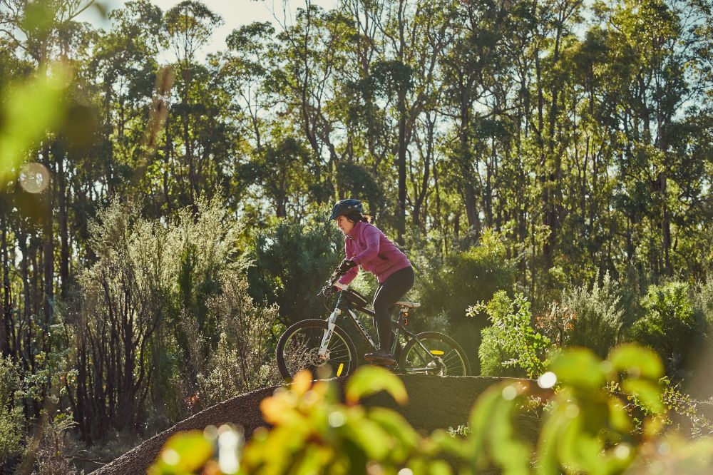A woman rides a bicycle down a ramp in the middle of the forest. 