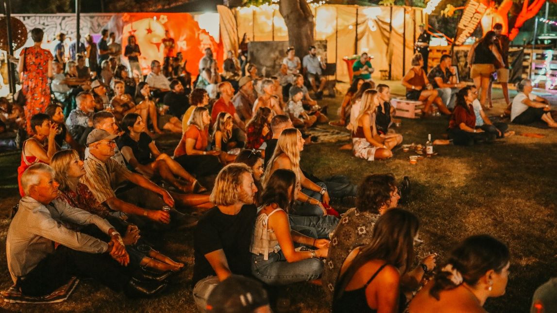 People sitting on the grass in the evening watching a show.