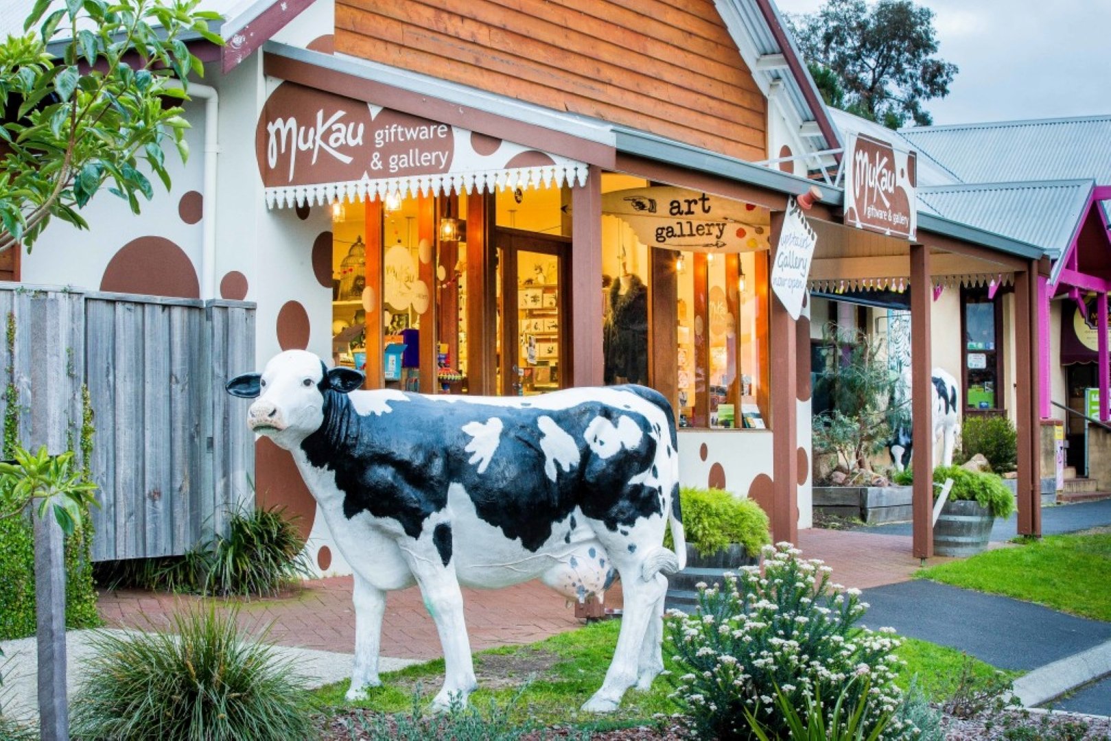 A cow statue stands on the street in front of a shop.