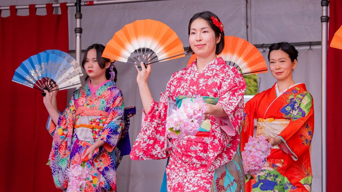 Women dressed up in kimonos on stage dancing with fans