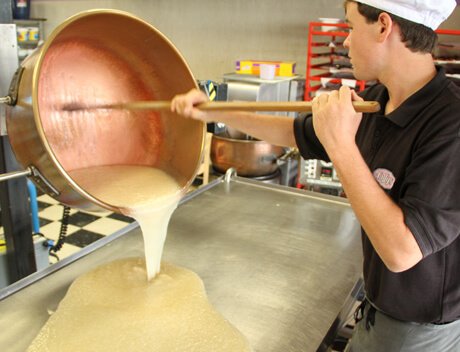 A man pouring hot taffy from a copper pot onto a pan